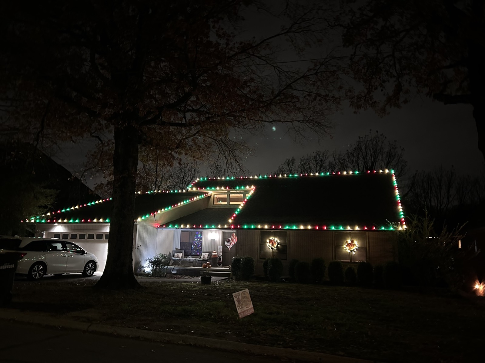Red and green roofline lighting on a Central Arkansas home with Pug Lights yard sign