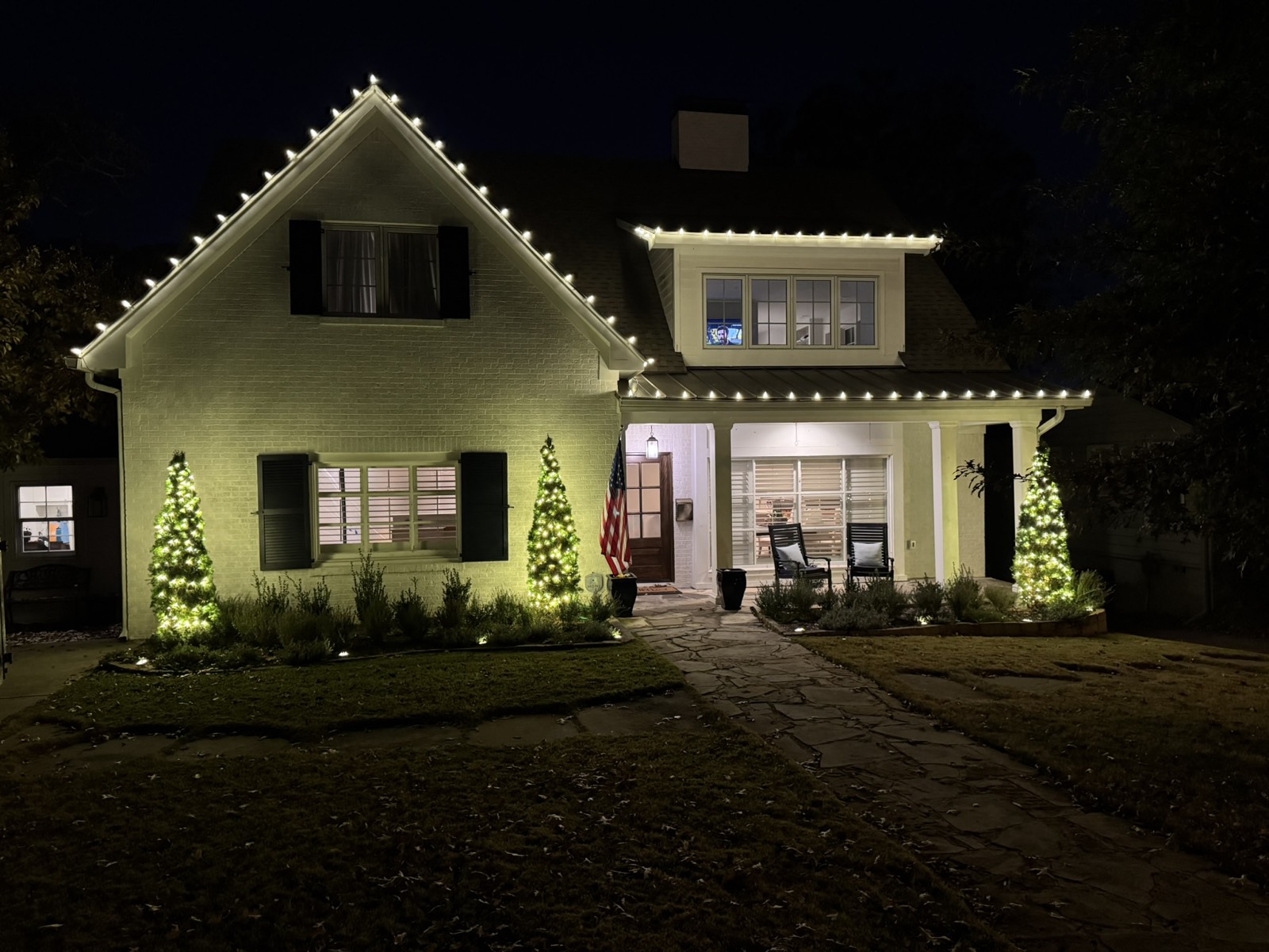 Home with roofline lighting and lit landscape cone trees flanking the entrance