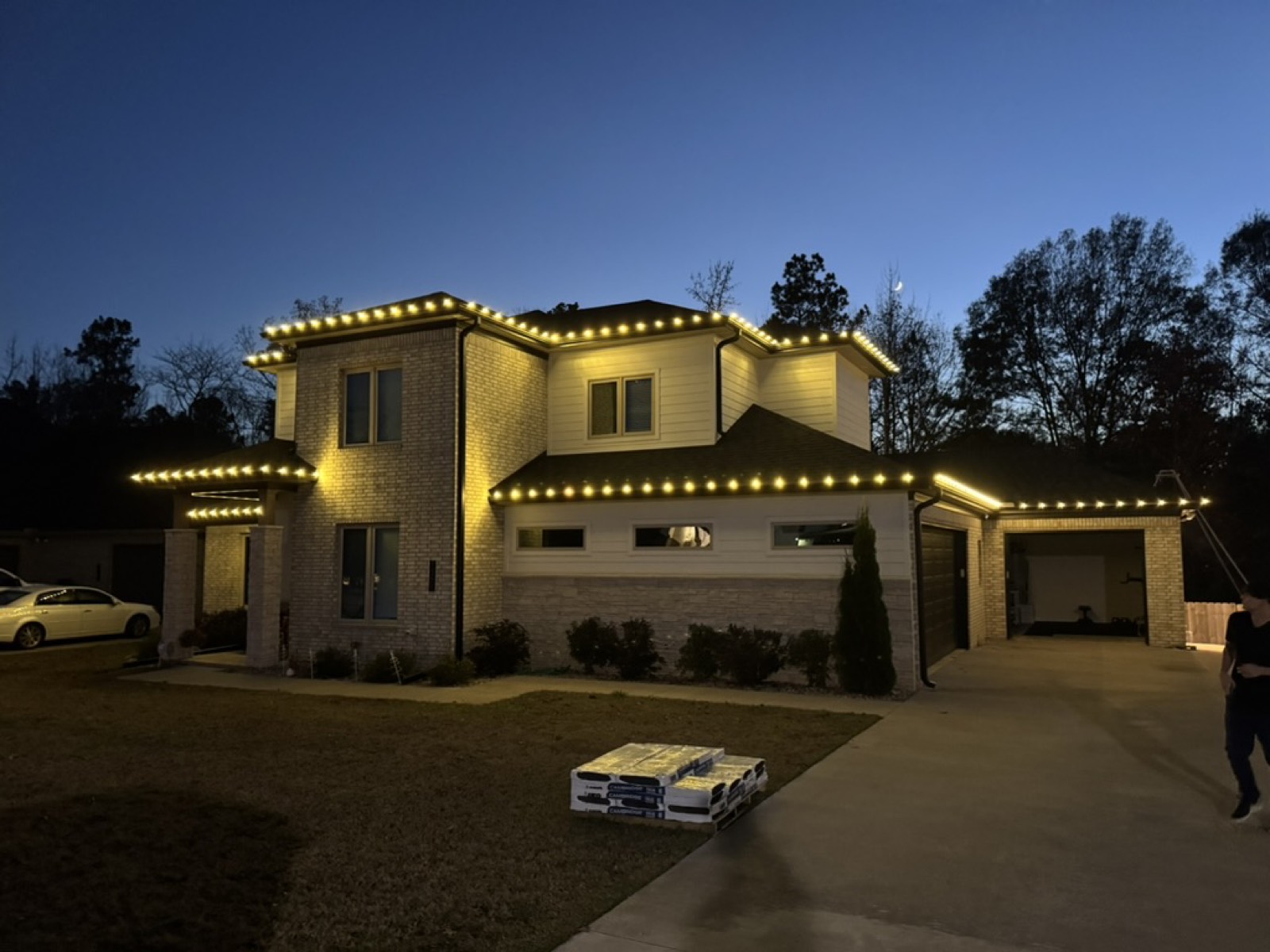 Two-story stone and brick home with roofline lighting at twilight